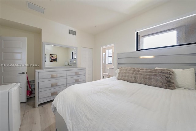 bedroom with light wood finished floors, visible vents, and ensuite bathroom