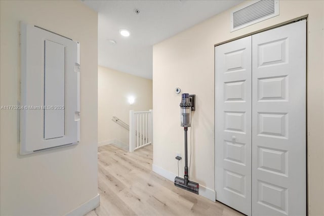 hallway with an upstairs landing, light wood finished floors, baseboards, visible vents, and recessed lighting