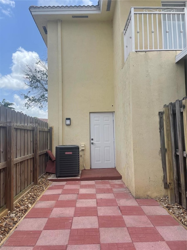 doorway to property featuring fence, stucco siding, and central air condition unit