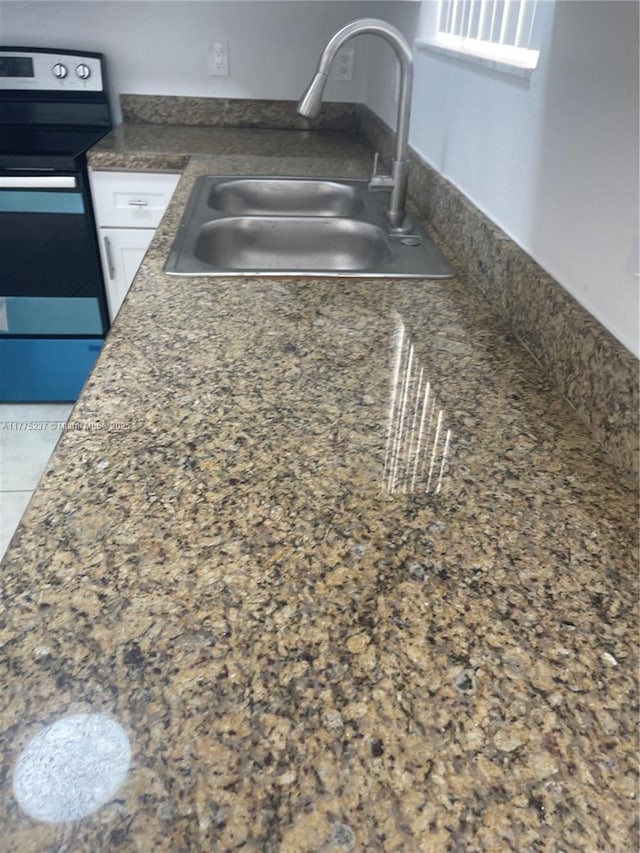 kitchen featuring dark countertops, stainless steel range with electric stovetop, white cabinetry, and a sink