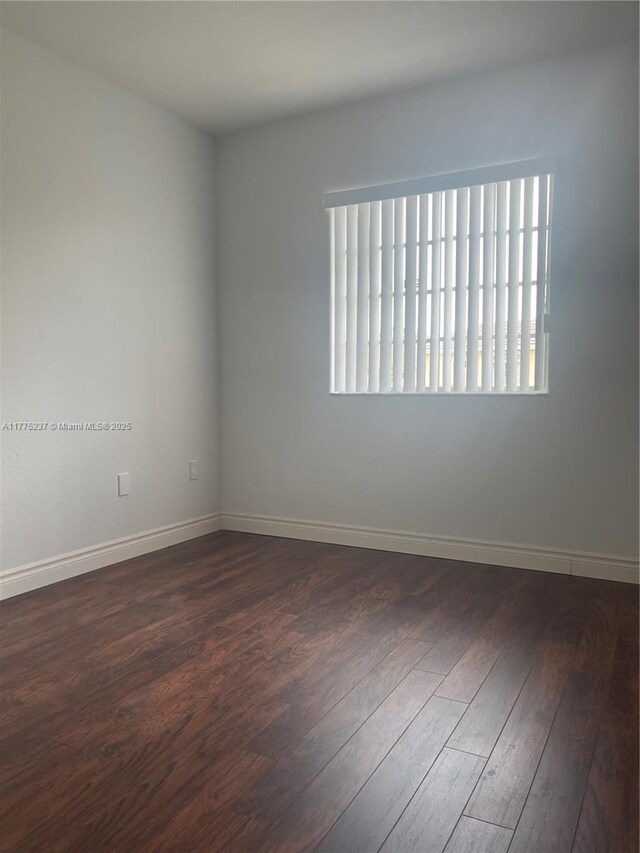 empty room with baseboards, a wealth of natural light, and dark wood-style flooring