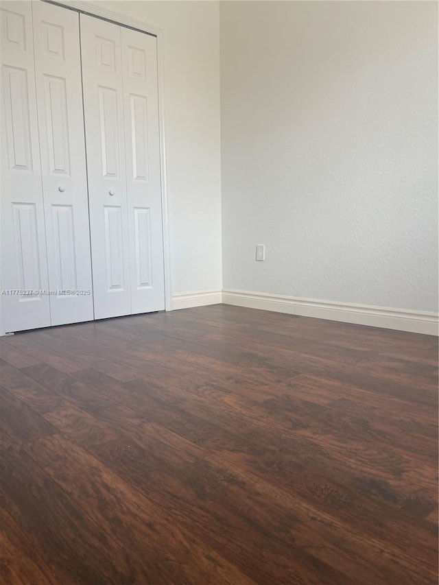 unfurnished bedroom with dark wood-type flooring, a closet, and baseboards