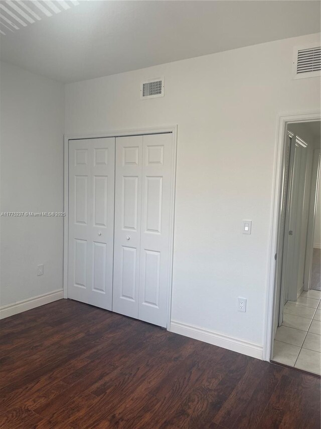 unfurnished bedroom with wood finished floors, visible vents, a closet, and baseboards