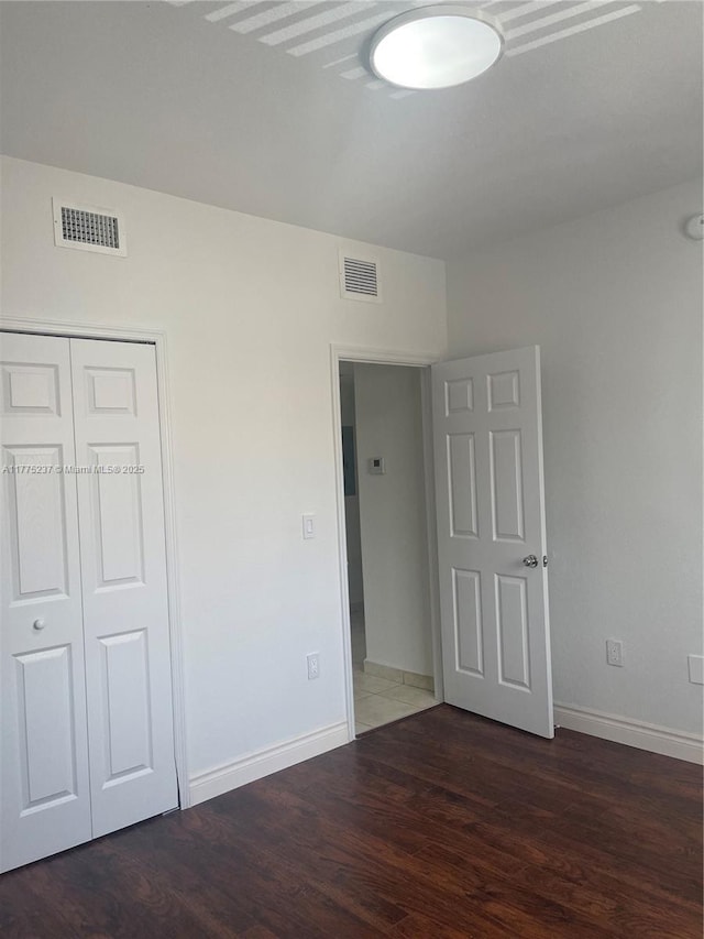 unfurnished bedroom with baseboards, visible vents, wood finished floors, and a closet