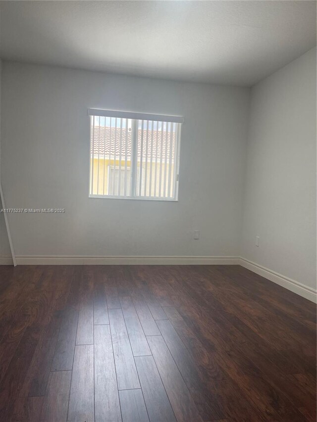 spare room featuring dark wood-style floors and baseboards