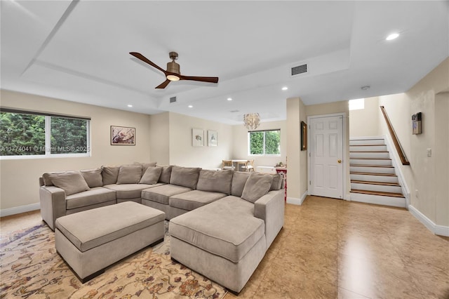 living room with a ceiling fan, a tray ceiling, stairway, and visible vents