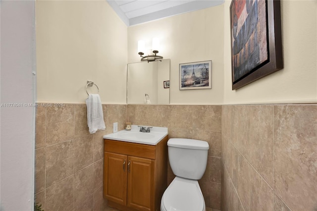 bathroom with a wainscoted wall, tile walls, toilet, and vanity