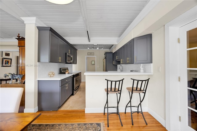 kitchen featuring a kitchen breakfast bar, light countertops, a peninsula, and appliances with stainless steel finishes