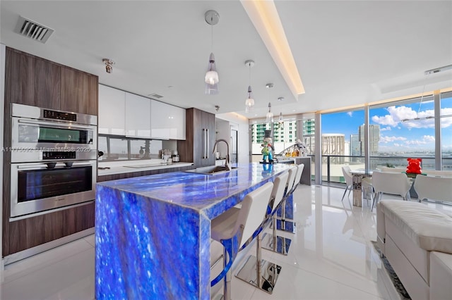 kitchen featuring modern cabinets, double oven, a sink, a large island, and light tile patterned floors