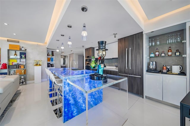 kitchen featuring modern cabinets, a sink, light tile patterned flooring, dark brown cabinets, and decorative light fixtures