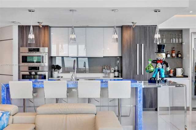 kitchen with modern cabinets, double oven, white cabinetry, light countertops, and a breakfast bar area