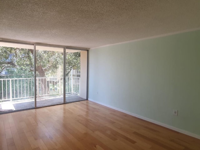 empty room featuring a wall of windows, a textured ceiling, wood finished floors, and baseboards