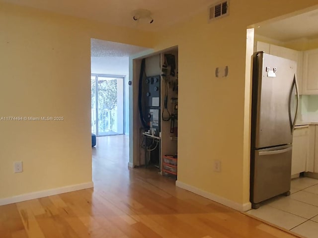 kitchen featuring freestanding refrigerator, white cabinets, light wood-type flooring, and baseboards