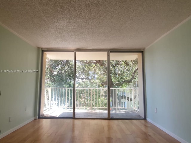 empty room featuring expansive windows, a textured ceiling, plenty of natural light, wood finished floors, and baseboards
