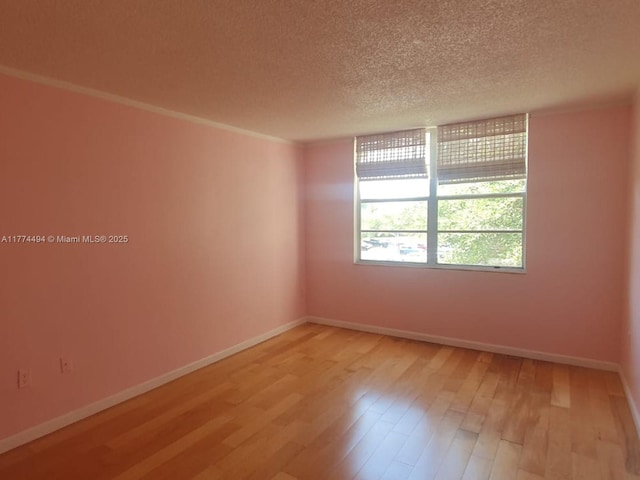 unfurnished room featuring a textured ceiling, light wood finished floors, and baseboards