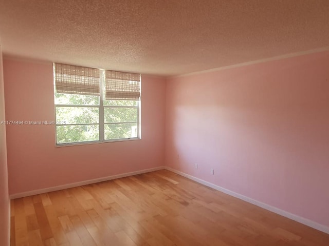 unfurnished room with a textured ceiling, light wood-type flooring, and baseboards