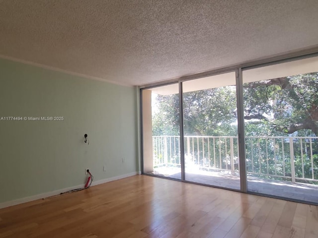 empty room with a wall of windows, a textured ceiling, wood finished floors, and baseboards