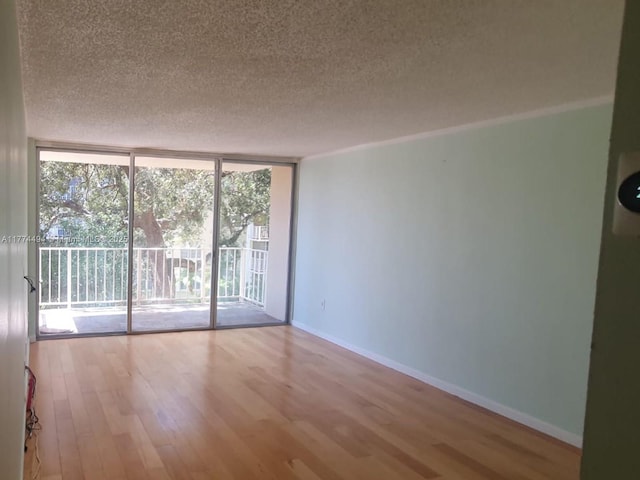 unfurnished room featuring a wall of windows, a textured ceiling, wood finished floors, and baseboards