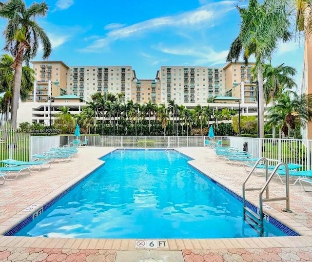pool with a patio, a view of city, and fence
