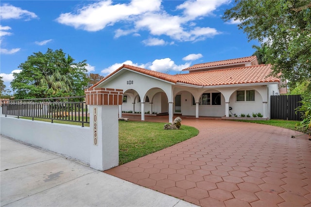 mediterranean / spanish-style house featuring curved driveway, stucco siding, fence, a front lawn, and a tile roof