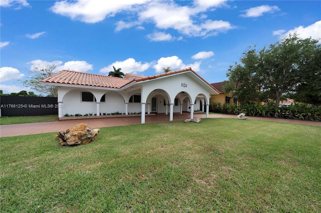mediterranean / spanish-style home featuring a tiled roof, stucco siding, fence, and a front lawn