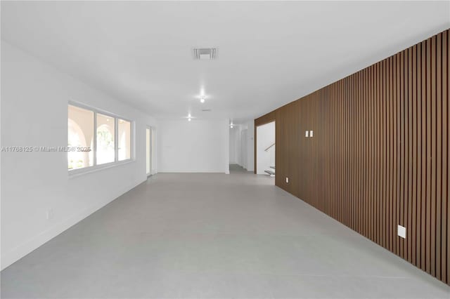unfurnished room featuring wood walls, concrete floors, visible vents, and stairway