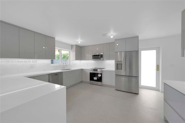 kitchen with modern cabinets, tasteful backsplash, appliances with stainless steel finishes, a sink, and gray cabinetry