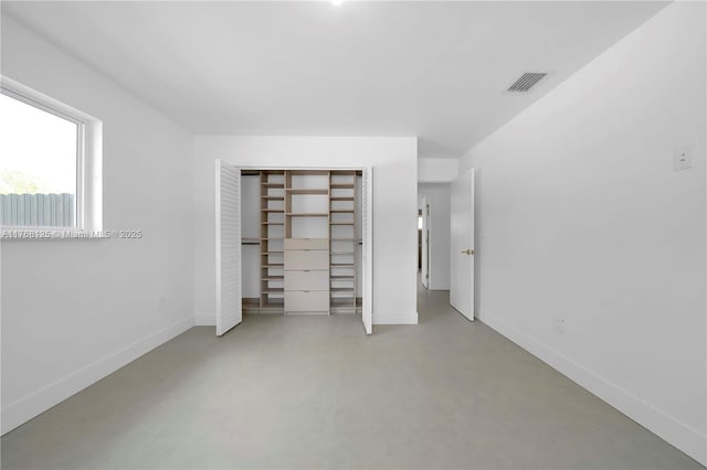 unfurnished bedroom featuring a closet, concrete flooring, baseboards, and visible vents