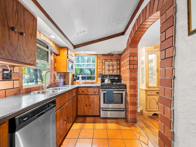 kitchen featuring a sink, tasteful backsplash, lofted ceiling, stainless steel appliances, and stainless steel counters