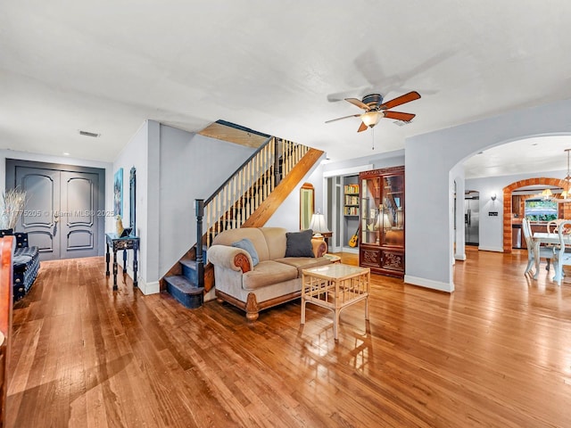 living room with arched walkways, stairs, a ceiling fan, and wood-type flooring