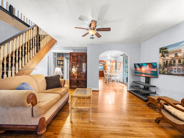 living room featuring stairs, arched walkways, visible vents, ceiling fan, and wood finished floors