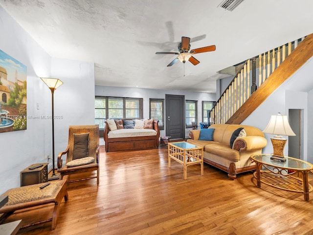 living area featuring wood-type flooring, ceiling fan, stairs, and visible vents