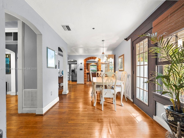 dining area with light wood finished floors, visible vents, a notable chandelier, and arched walkways
