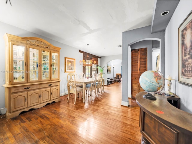 interior space featuring a chandelier, light wood finished floors, baseboards, visible vents, and arched walkways