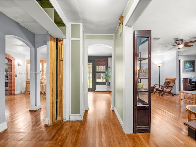hall with baseboards, wood finished floors, and arched walkways