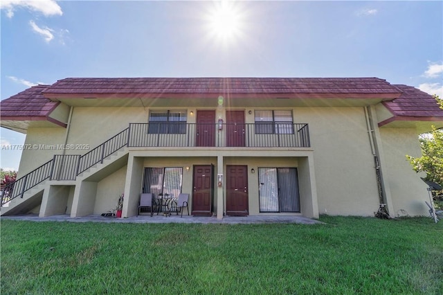 rear view of property featuring a balcony, stucco siding, stairway, and a yard