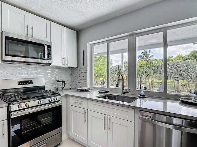 kitchen featuring decorative backsplash, a textured ceiling, appliances with stainless steel finishes, a sink, and white cabinets