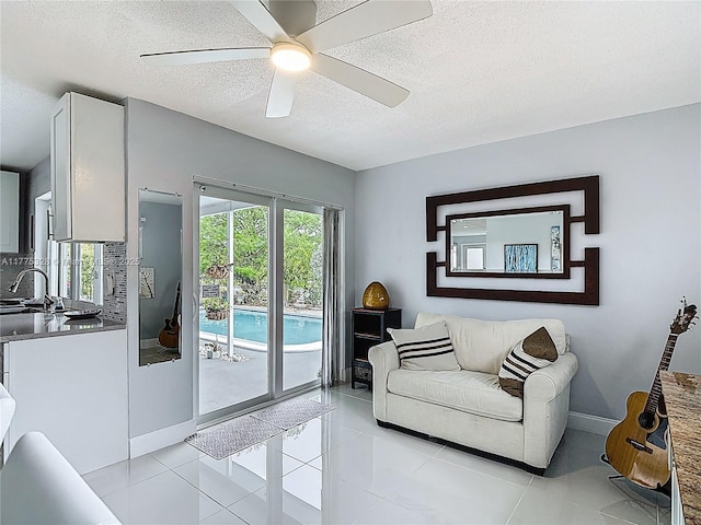 living area with baseboards, a ceiling fan, a textured ceiling, and light tile patterned flooring