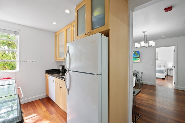 kitchen with baseboards, an inviting chandelier, dark countertops, white appliances, and wood finished floors