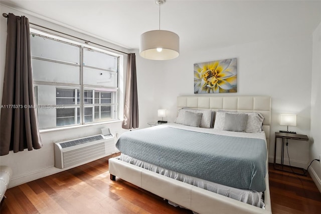 bedroom featuring baseboards, wood finished floors, and a wall mounted air conditioner