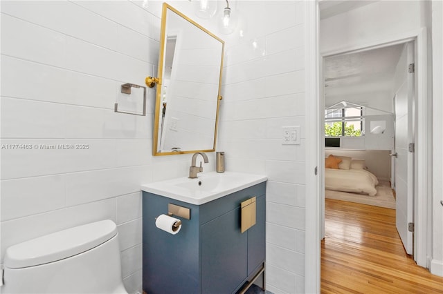 half bath featuring vanity, tile walls, toilet, and wood finished floors