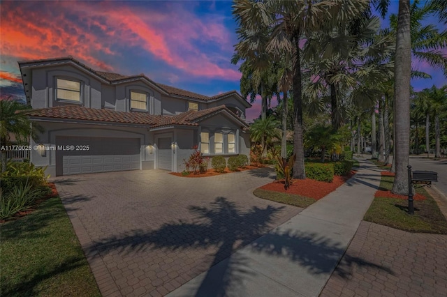 mediterranean / spanish-style house with stucco siding, decorative driveway, an attached garage, and a tile roof