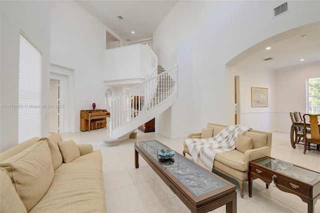 living area featuring visible vents, light tile patterned floors, arched walkways, a high ceiling, and stairs