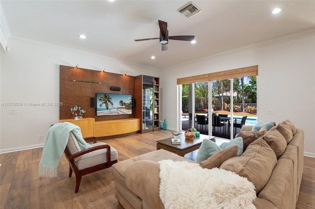 living room with baseboards, a ceiling fan, crown molding, visible vents, and wood finished floors