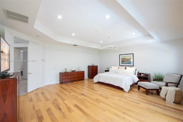 bedroom with visible vents, light wood-type flooring, a raised ceiling, and recessed lighting