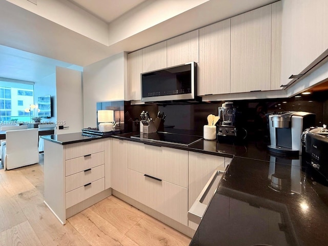 1331 Brickell Bay Dr Unit 506, Miami, FL 33131 - kitchen with stainless steel microwave, black electric stovetop, a peninsula, light wood-style floors, and dark countertops