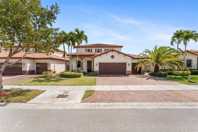 mediterranean / spanish-style house featuring stone siding, a tile roof, decorative driveway, and a garage