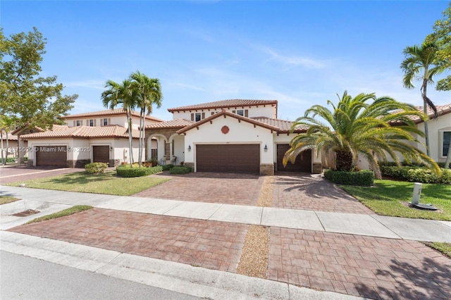 mediterranean / spanish-style house featuring a tile roof, a front yard, stucco siding, decorative driveway, and a garage