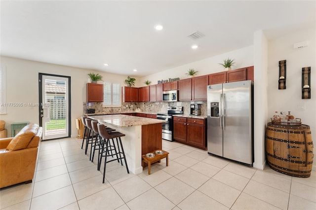 kitchen with light stone counters, a kitchen breakfast bar, appliances with stainless steel finishes, visible vents, and decorative backsplash