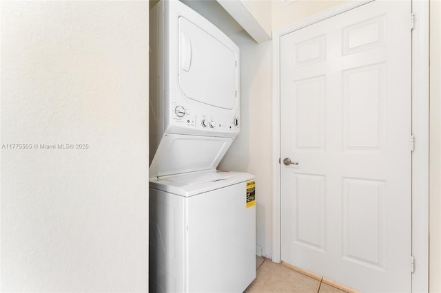 clothes washing area featuring light tile patterned flooring, stacked washing maching and dryer, and laundry area